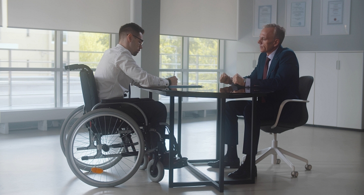 Disabled businessman in wheelchair and lawyer sitting at table and sign documents in modern office