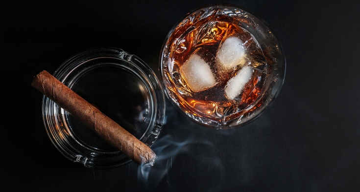 Glass of cold whiskey with cigar on dark background