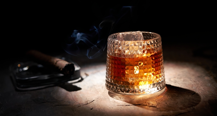 Glass of whiskey and smoking cigar on table. Copy space, black background. Whiskey, brandy, cognac, alcoholic drink .