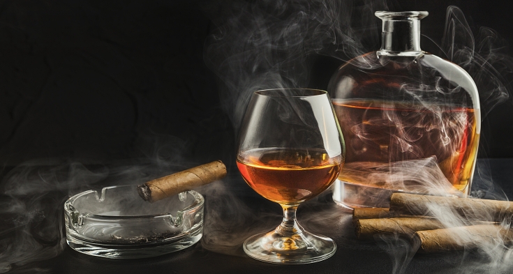 Glass of whiskey with smoking cigar and ibottle on black background, copy space