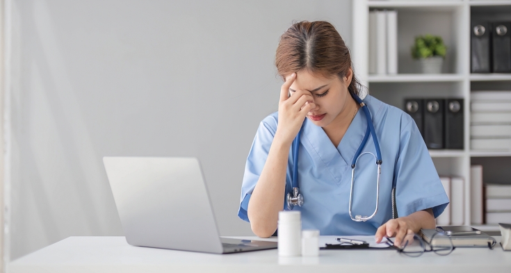 Stressed young female doctor looking at laptop reading bad news online worried of mistake at workplace. Unhappy professional physician in tension feeling tired solving computer problem at work.